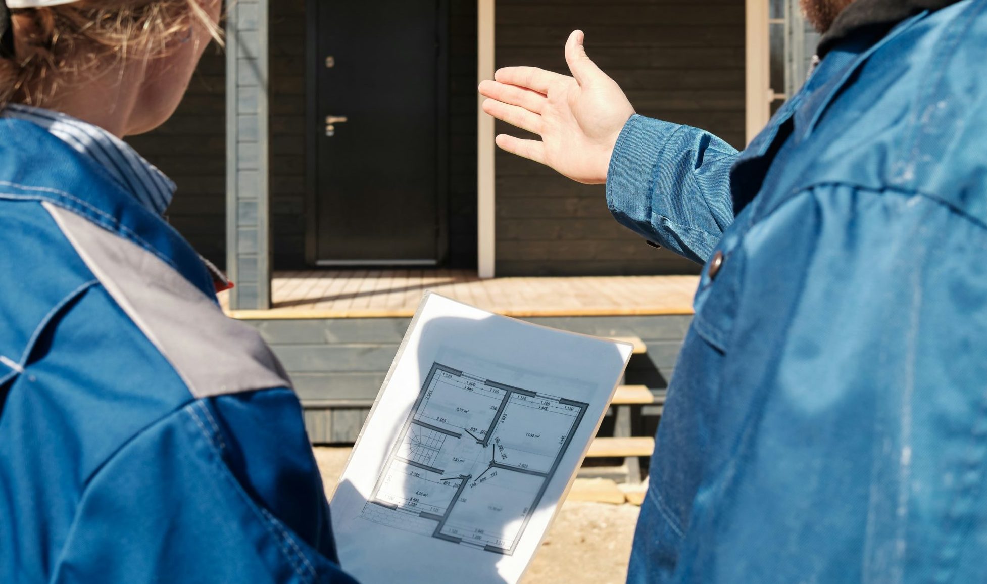 Une femme, tenant les plans d'une maison, et un homme, montrant le porche d'une maison, de dos.