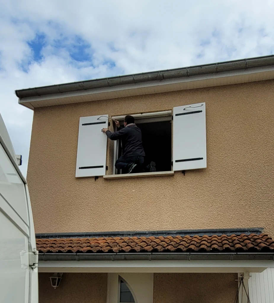 Un installateur réglant l'attache d'un volet battant depuis l'intérieur